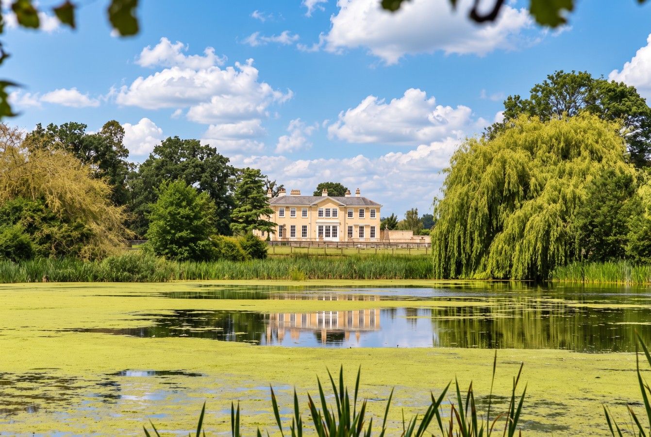 A large building with a reflection in a pond, surrounded by trees and greenery.