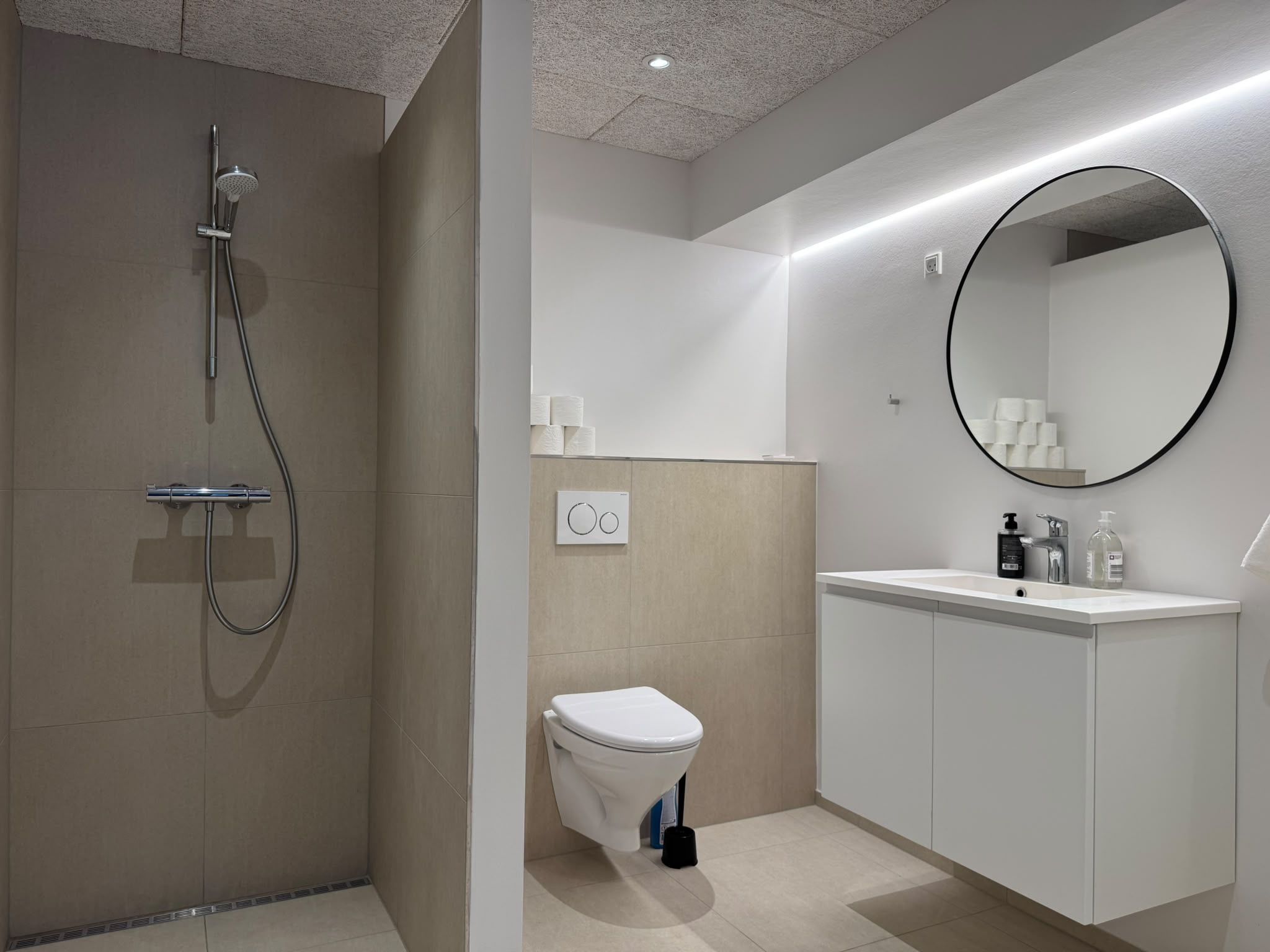 A modern bathroom with a shower, toilet, sink, and a large mirror.