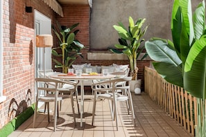 An outdoor patio with a round table and chairs, surrounded by potted plants and a brick wall. - New Listing (Madrid)