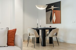 A modern dining area with a round table, two chairs, a pendant light, and a painting on the wall. - New Listing (Madrid)