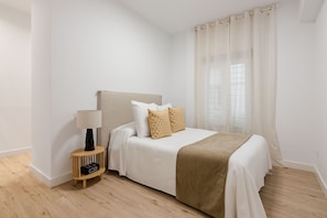 A bedroom with a bed, a bedside table with a lamp, and a window with curtains. - New Listing (Madrid)