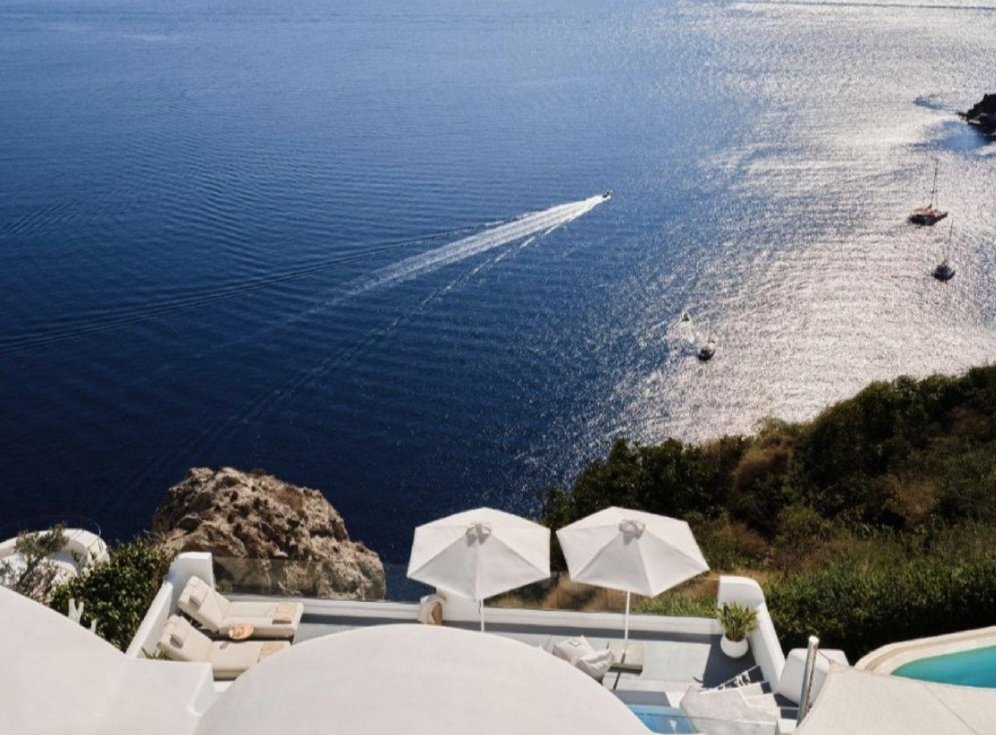 Un espace piscine doté de chaises longues et de parasols, avec vue sur une étendue d’eau où se trouvent des bateaux.