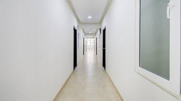 Un pasillo largo y estrecho con paredes y puertas blancas a ambos lados, que conduce a una habitación luminosa al final.