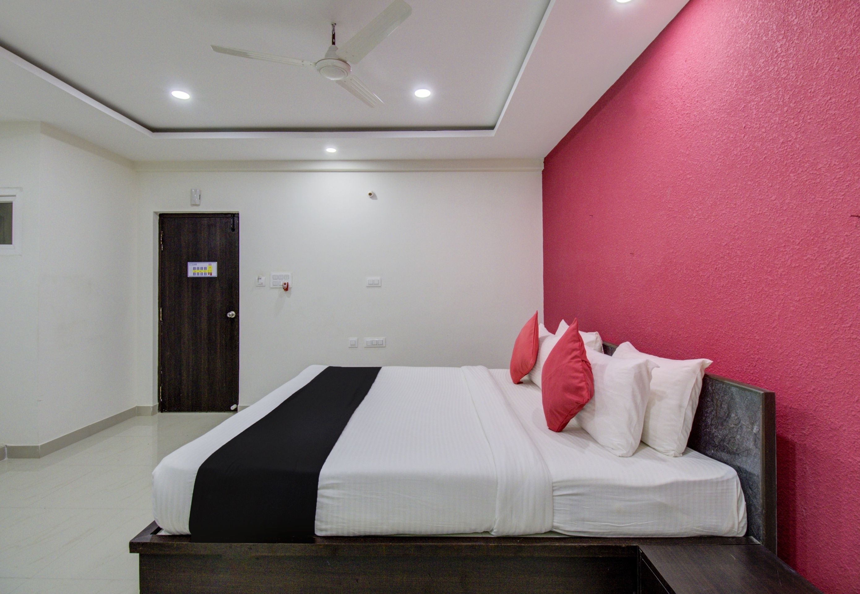 Habitación de hotel con cama, ventilador de techo y una pared de acento roja.
