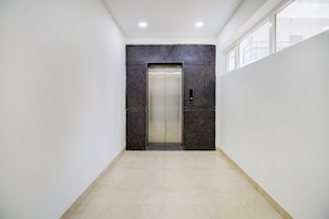A hallway with a marble wall and a door leading to an elevator. - Super Hotel O by OYO 75327 Atithi (Bangalore)