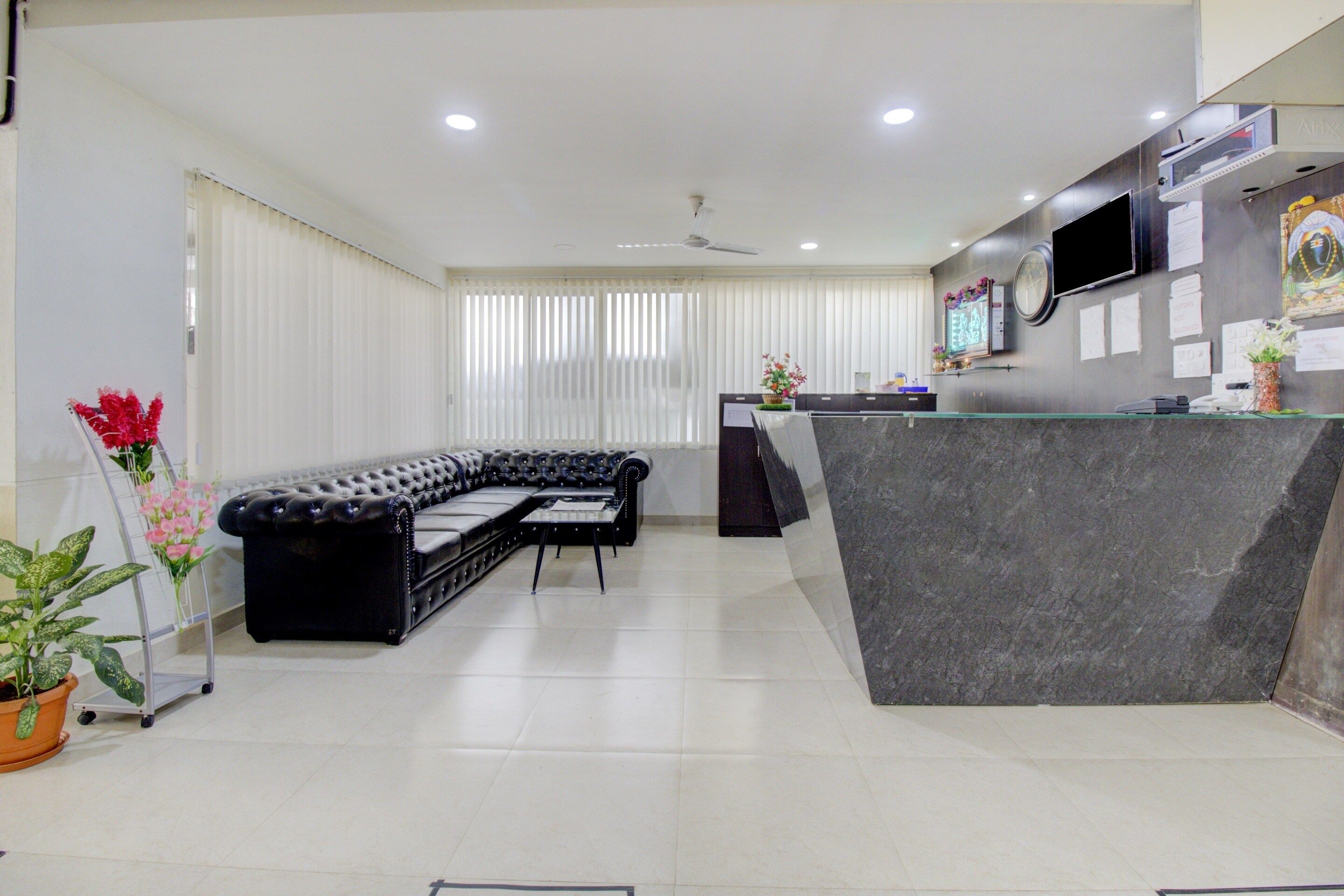 Una moderna zona de recepción con un sofá de cuero negro, un mostrador de recepción de mármol y un televisor de pantalla plana montado en la pared.