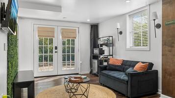 A modern living room with a dark grey sofa, a round coffee table, and a large window with blinds.