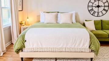 A bed with a green and white bedspread, a bedside table with a lamp, and a green sofa.