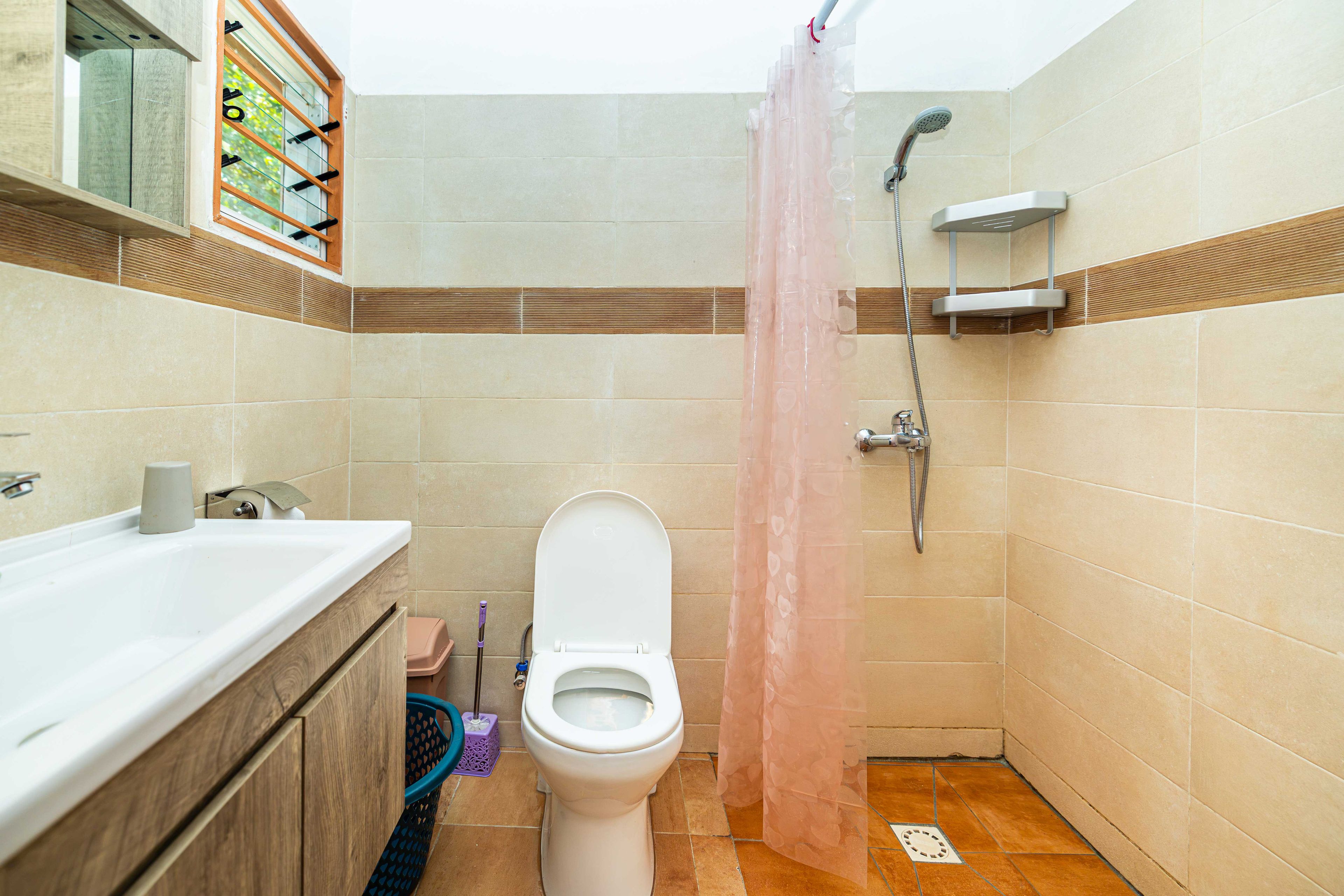 A bathroom with a toilet, sink, shower, and a window with blinds.