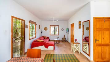 Habitación con cama, una mesa y una silla. Se ve follaje a través de la ventana.