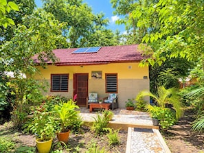 A house with a red tiled roof, solar panels, a tiled patio, and lush greenery. - Busy Bee Nature Residence (Mariama Kunda)