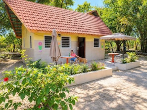 A house with a tiled roof, a patio with a table and chairs, and a dog. - Busy Bee Nature Residence (Mariama Kunda)