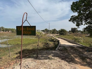 A sign for Tjizee Krook Bridge in a rural setting with a dirt path leading to a bridge.