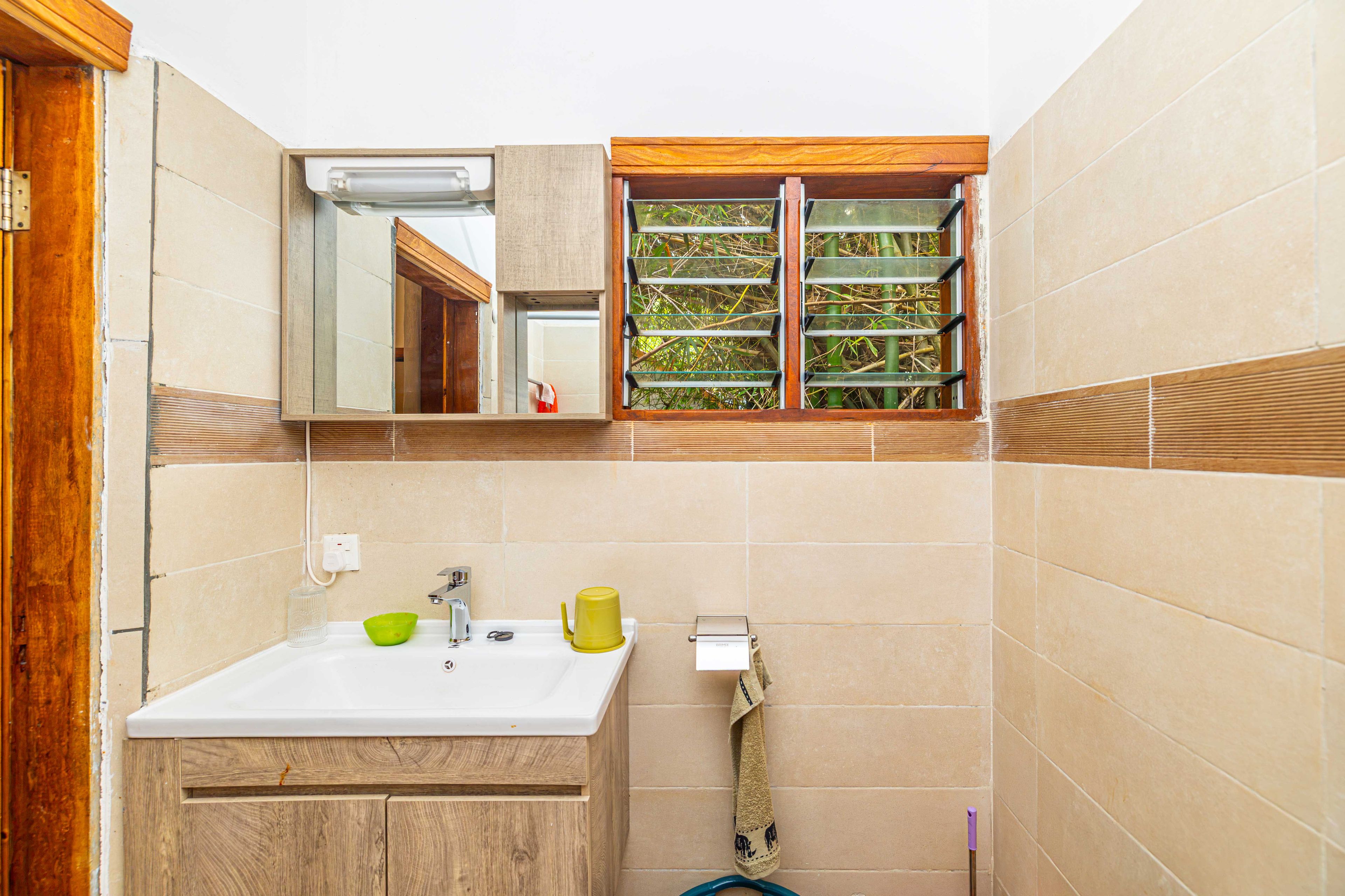 Un baño con tocador de madera, un espejo, una ventana con vistas a zonas verdes y un perchero.