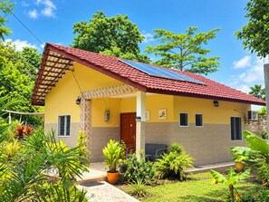 A two-story house with a red-tiled roof, solar panels, and a garden with various plants.