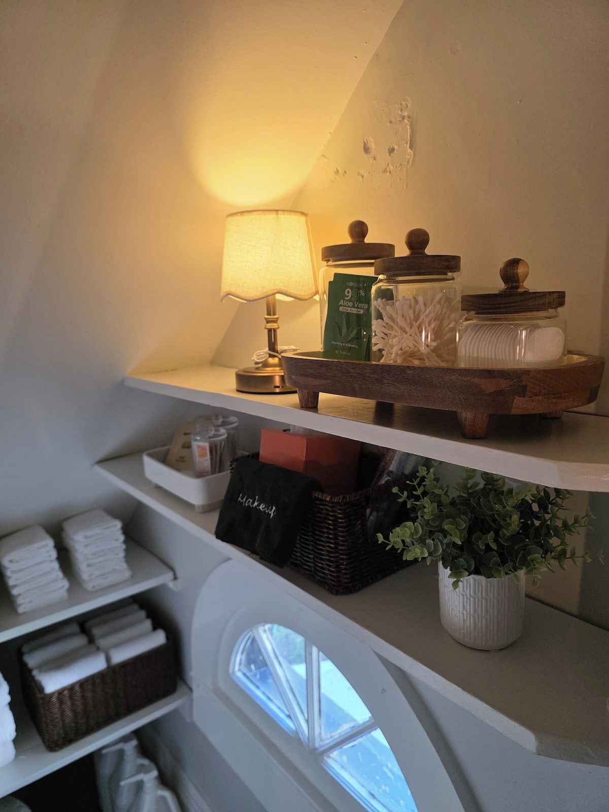 En hylde med en lampe, en aloe vera-flaske og en beholder med vatteknopper.
