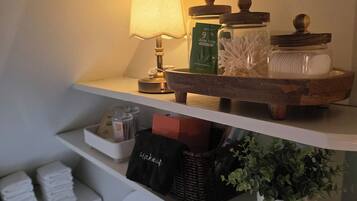 En hylde med en lampe, en aloe vera-flaske og en beholder med vatteknopper.