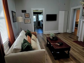 Un saló amb un sofà, una taula de centre i una televisió. Hi ha una porta que dona a una cuina i un passadís.