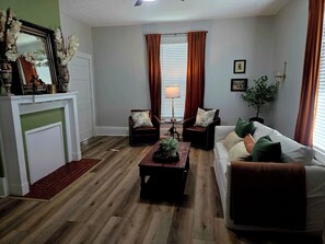 Una sala de estar con chimenea, dos sillones, un sofá, una mesa de centro y una lámpara.