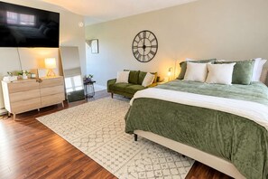 Ein Schlafzimmer mit Bett, Kommode, Fernseher und Wanduhr.