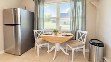 A kitchen with a stainless steel refrigerator, a wooden dining table with two chairs, and a trash bin.