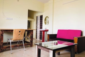 Une pièce comprenant une chaise en bois, une table avec un plateau en verre, un canapé rose, un miroir et une porte donnant sur une autre pièce.