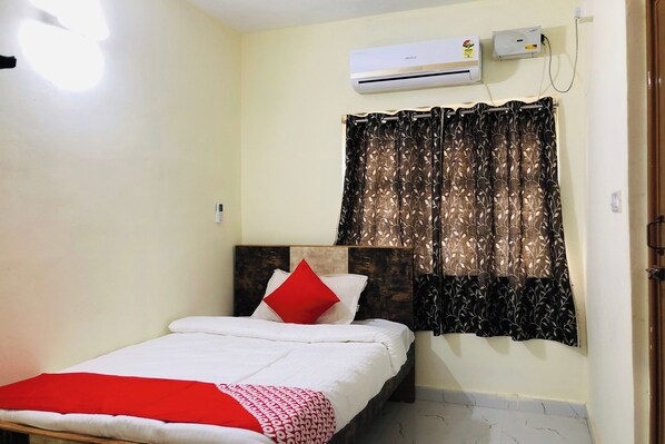 Une chambre à coucher avec un lit, un oreiller rouge, une couverture blanche et une fenêtre ornée de rideaux à motifs.
