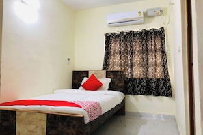 Quarto com cama, janela com cortinas estampadas, ar condicionado e luminária fixada na parede.