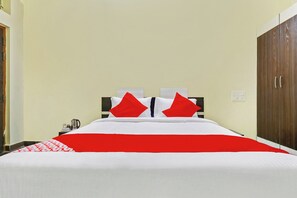 A hotel room with a bed, a nightstand, a wardrobe, and a wall-mounted light switch. - Hotel O JP PALACE (Doddaballapura)