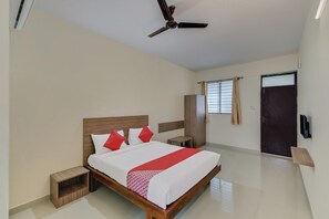 A modern hotel room with a large bed, a ceiling fan, a wardrobe, and a window with curtains. - Hotel O NCR Rooms (Bangalore)