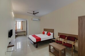A hotel room with a bed, a desk, a chair, a bedside table, a telephone, and a ceiling fan. - Hotel O NCR Rooms (Bangalore)