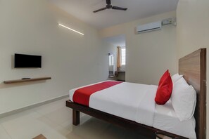 A hotel room with a bed, a television, an air conditioning unit, and a ceiling fan. - Hotel O NCR Rooms (Bangalore)