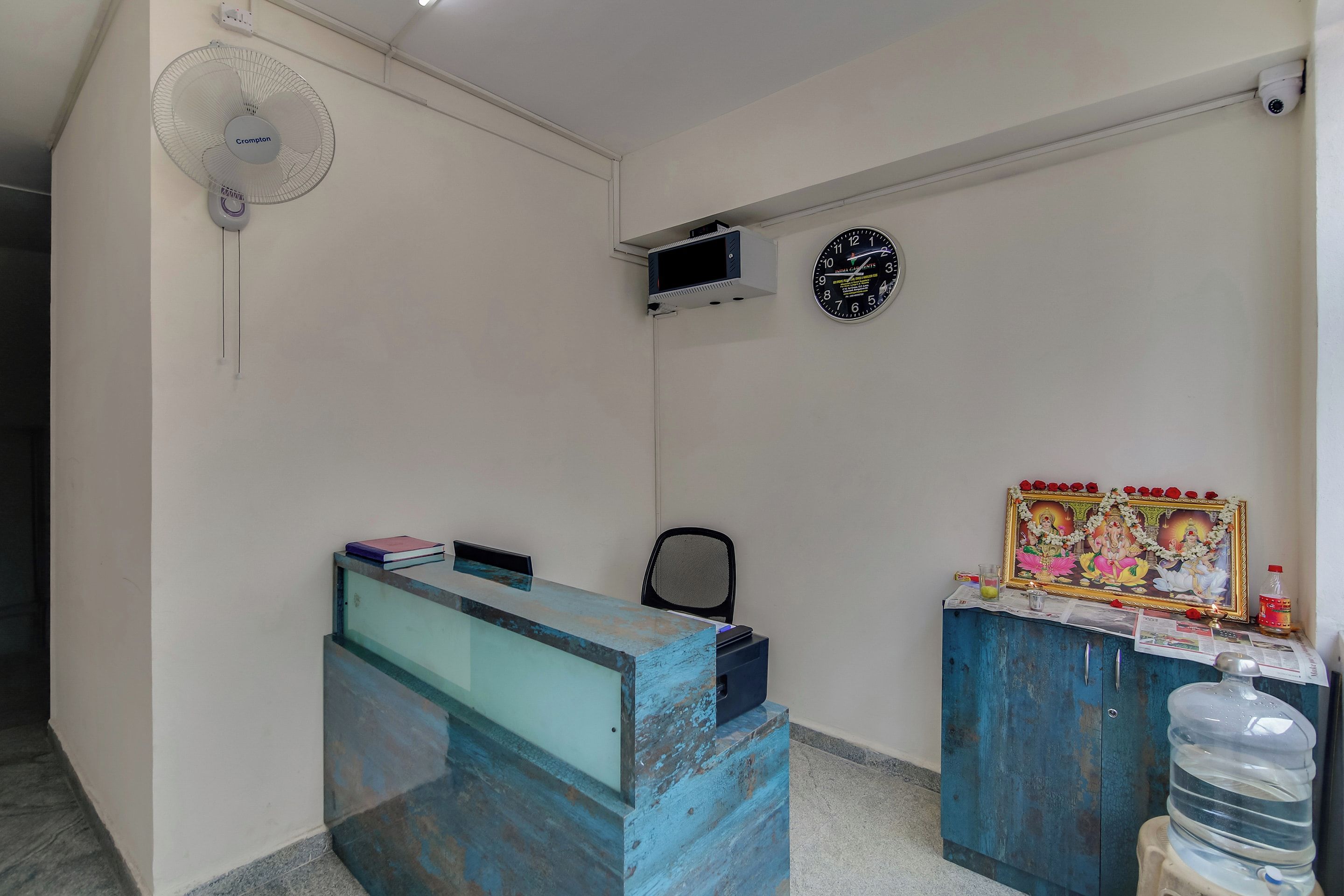 A reception area with a desk, a chair, a clock, a fan, and a water dispenser.