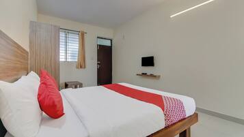 A hotel room with a bed, a television, and a window with blinds.