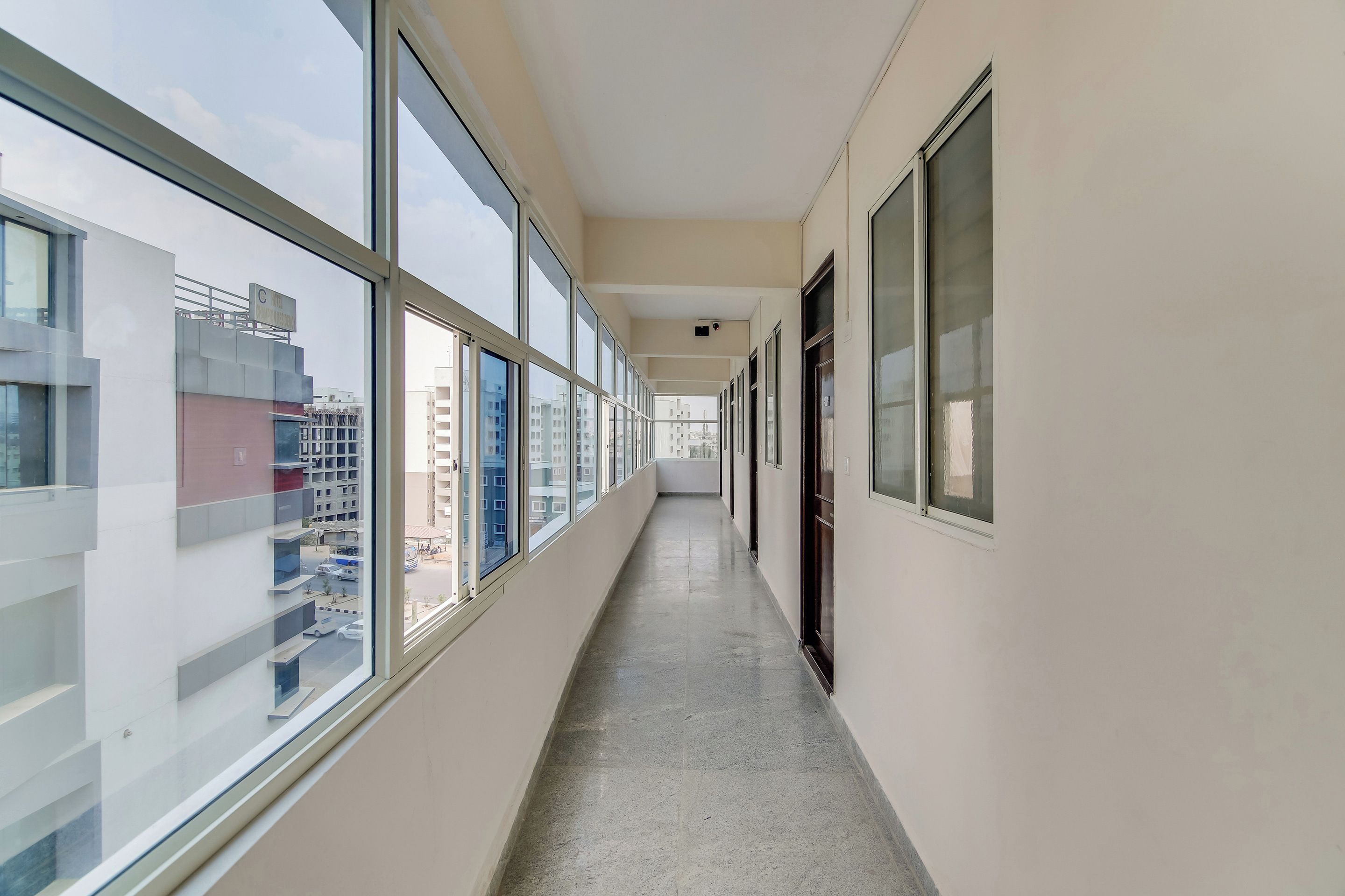 A corridor with large windows on one side, leading to a door on the other.