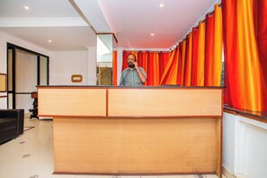 Un hombre está de pie frente a la recepción, con cortinas rojas en una habitación con paredes blancas y piso de baldosas.