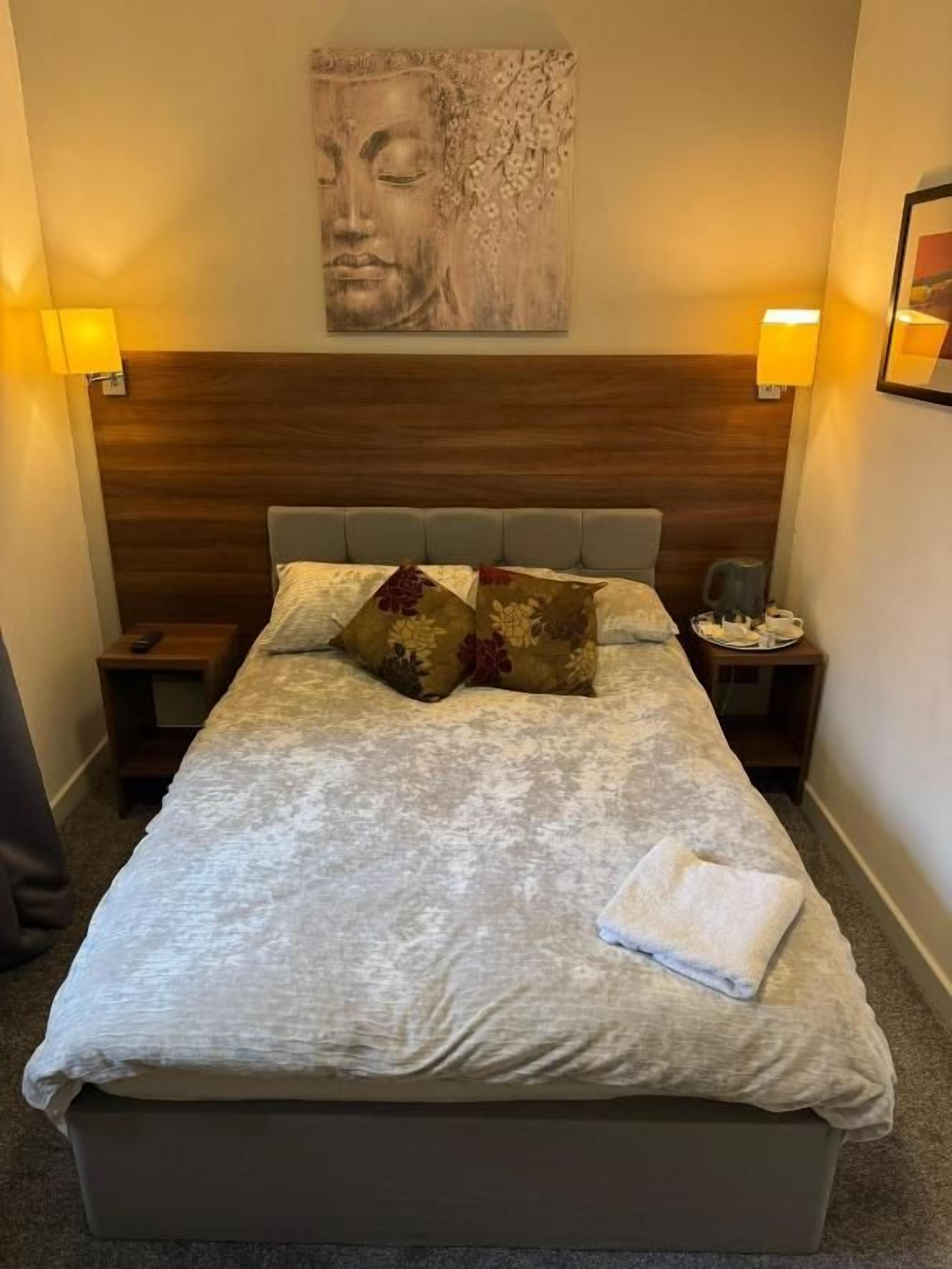 Ein Hotelzimmer mit einem großen Bett, zwei Nachttischen, einem Kopfteil und einem an der Wand befestigten Kunstwerk.