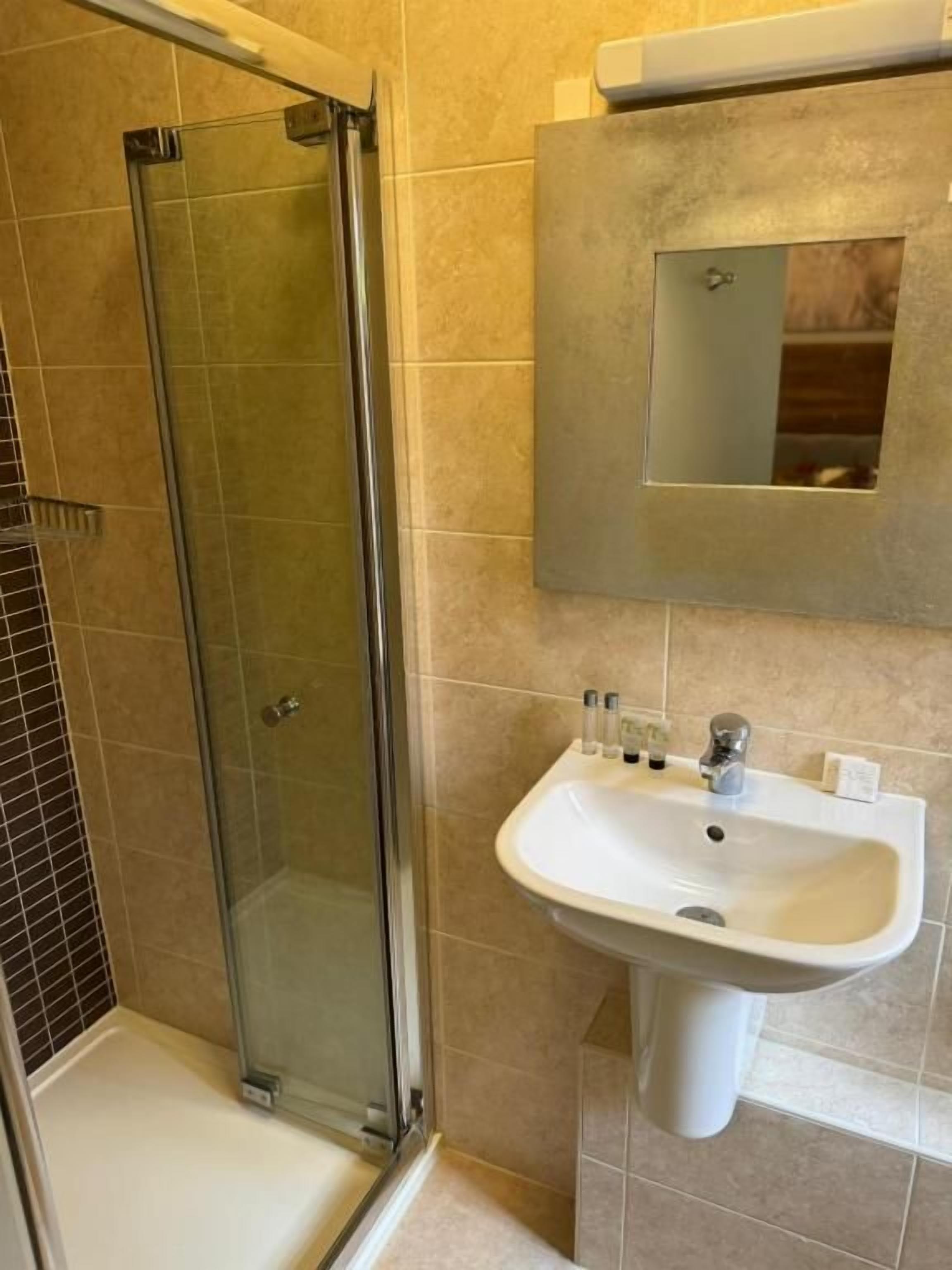 Un bany amb un plat de dutxa de vidre, un lavabo blanc i un mirall sobre el lavabo.