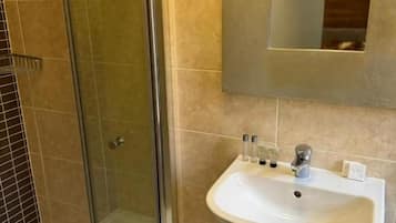 Un baño con cabina de ducha de vidrio, un lavabo blanco y un espejo sobre él.