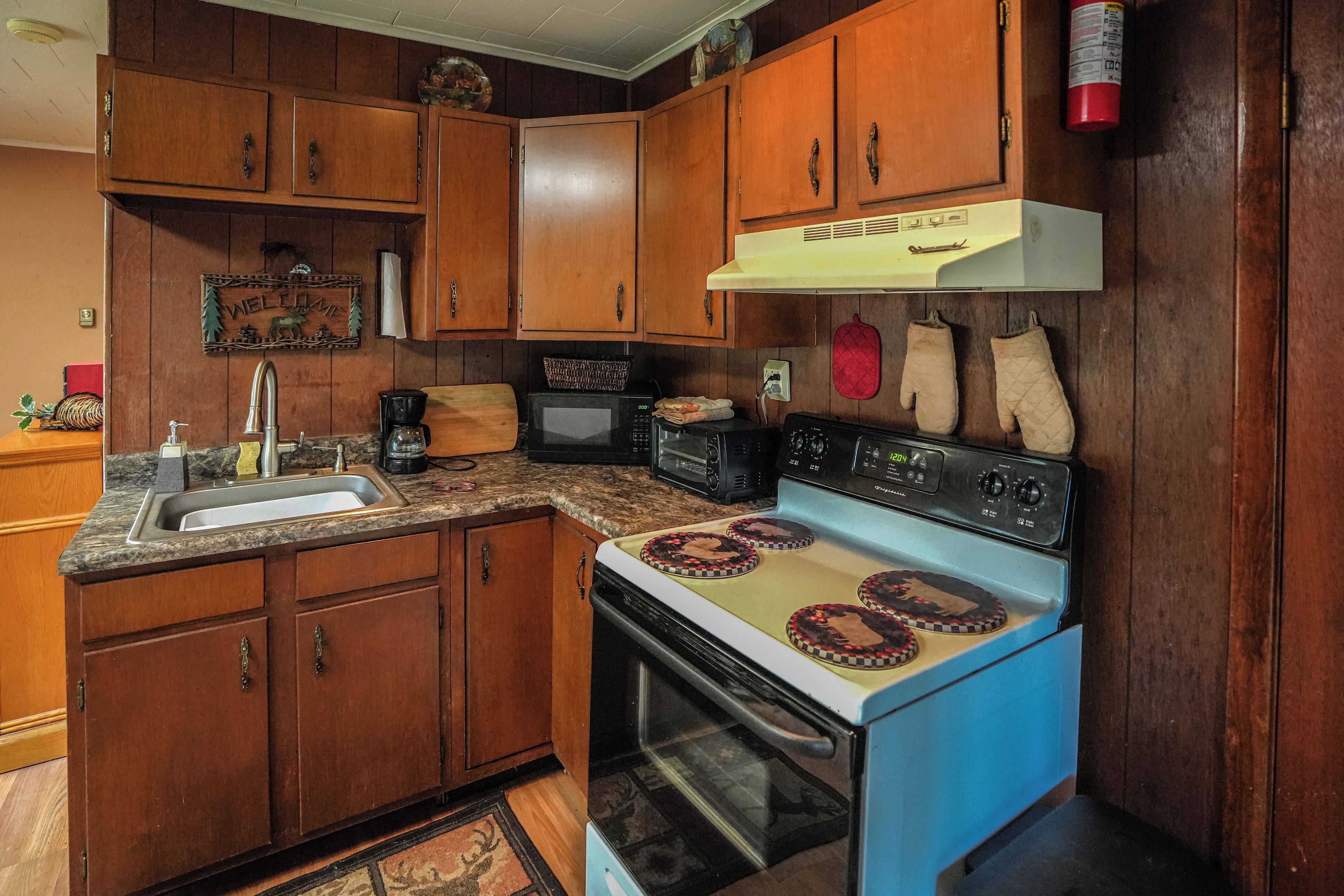 Una cocina con gabinetes de madera, estufa, microondas y un lavamanos.