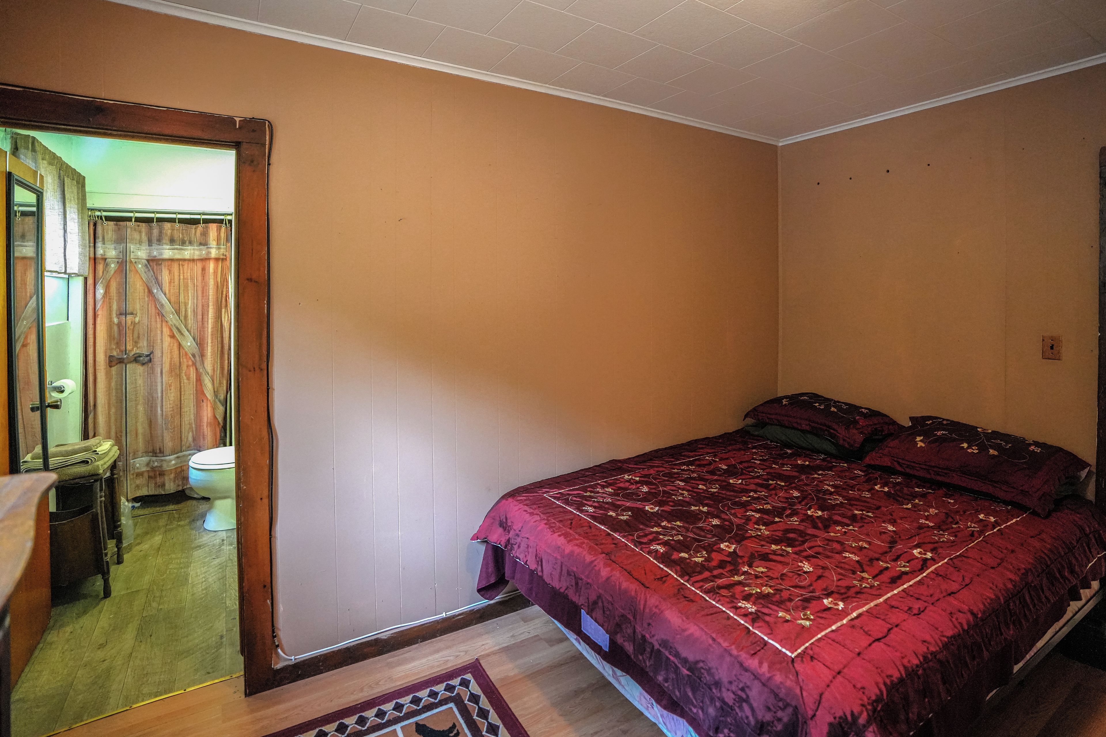 Un dormitorio con una cama individual, una puerta de madera y un baño pequeño visible a través de la puerta.