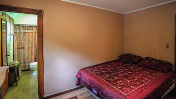 Un dormitorio con una cama individual, una puerta de madera y un baño pequeño visible a través de la puerta.