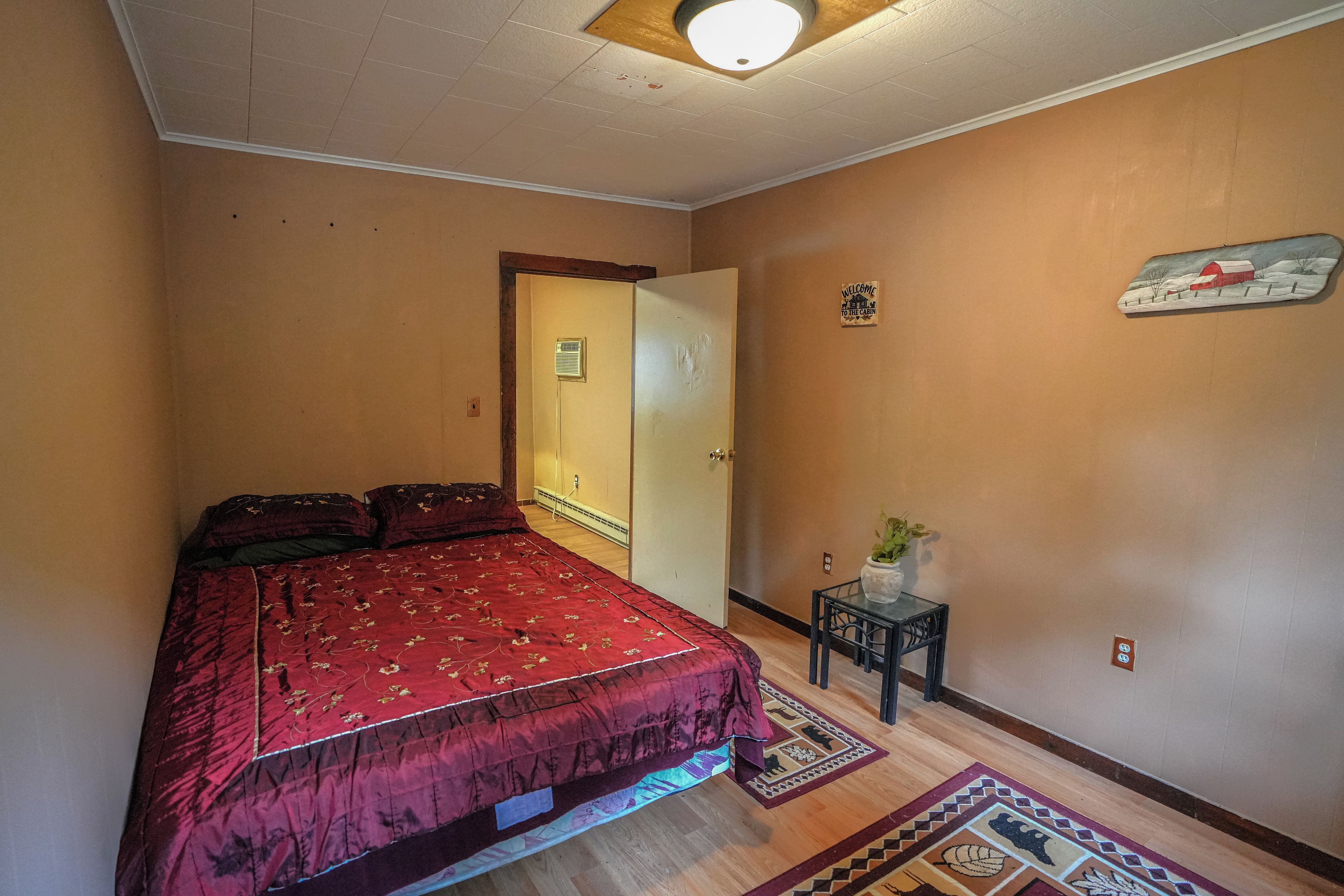 Un dormitorio con una cama, una mesita con una planta, un radiador y una puerta con un letrero.