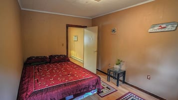 Un dormitorio con una cama, una mesita con una planta, un radiador y una puerta con un letrero.