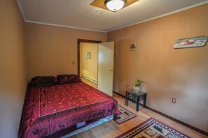 A bedroom with a bed, a small table with a plant, a radiator, and a door with a sign. - Adirondack Mountain Lakefront (Northville)