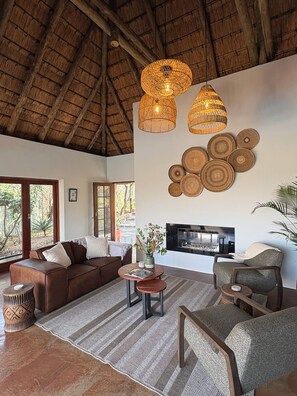 Amplia sala de estar con techo alto, chimenea y ventana grande con vista a un paisaje natural.