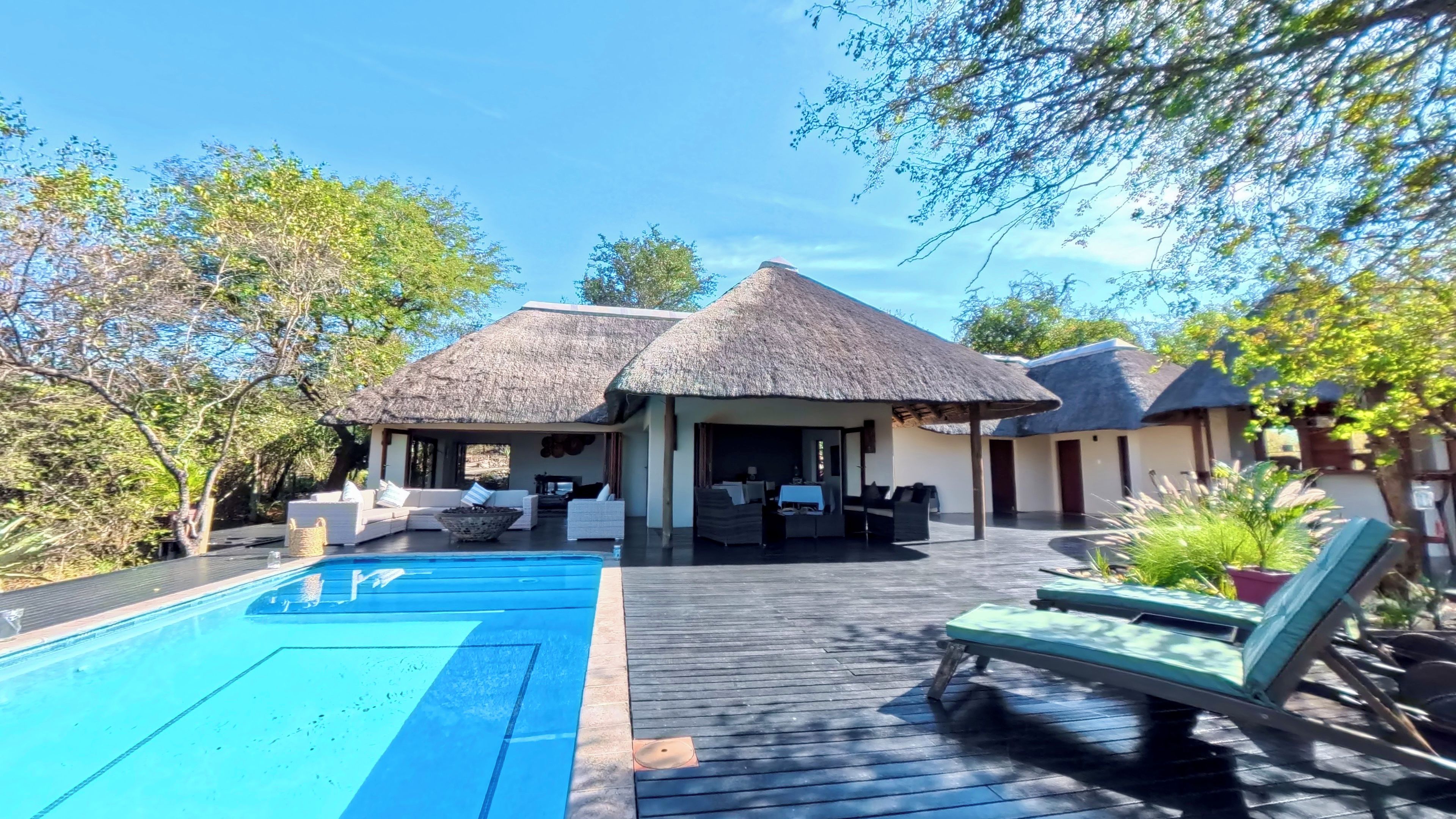 Un espace aménagé au bord de la piscine, avec des structures à toits de chaume, des chaises longues et une terrasse en bois.