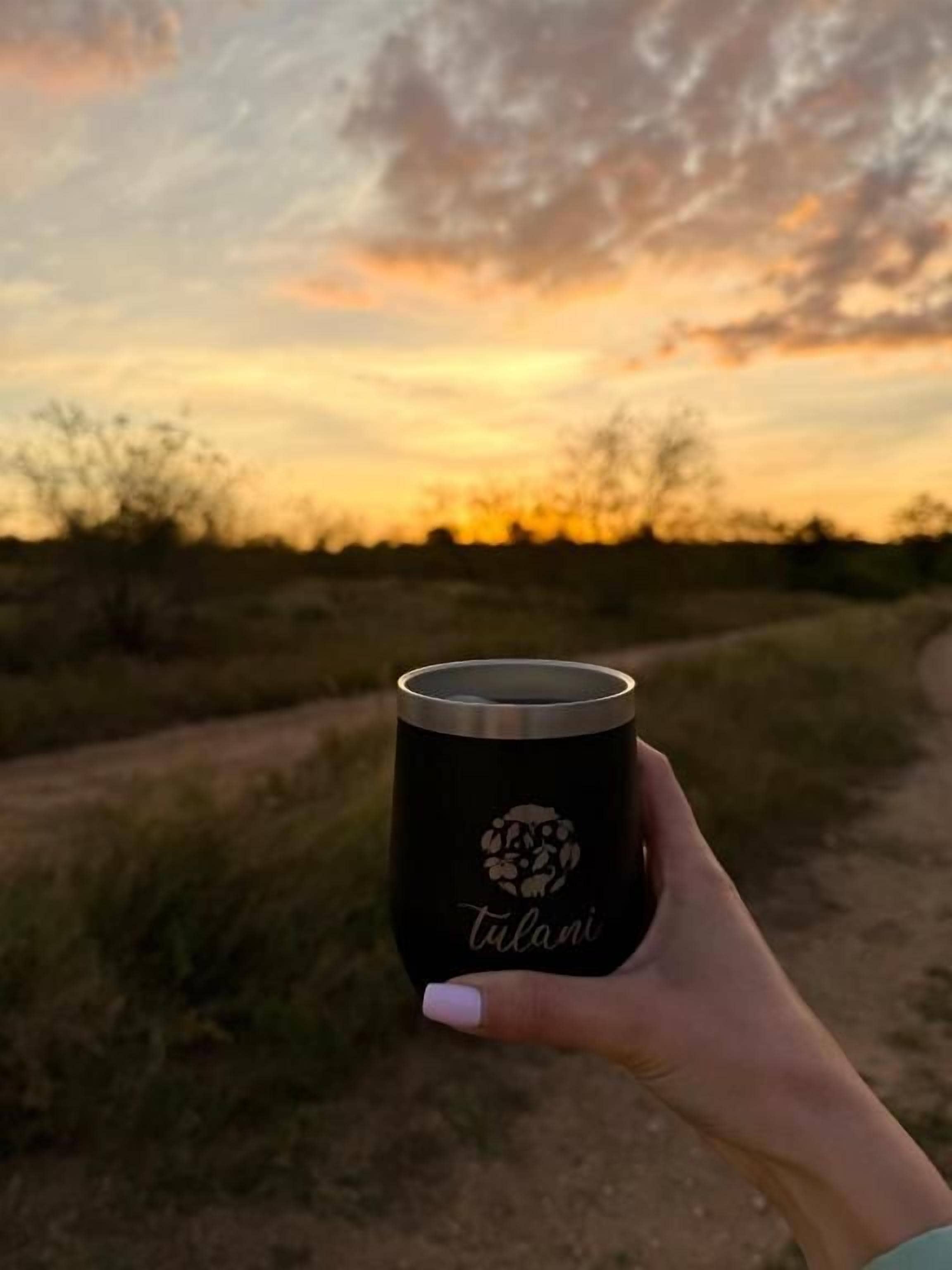 A hand holding a mug with a logo, set against a sunset background.