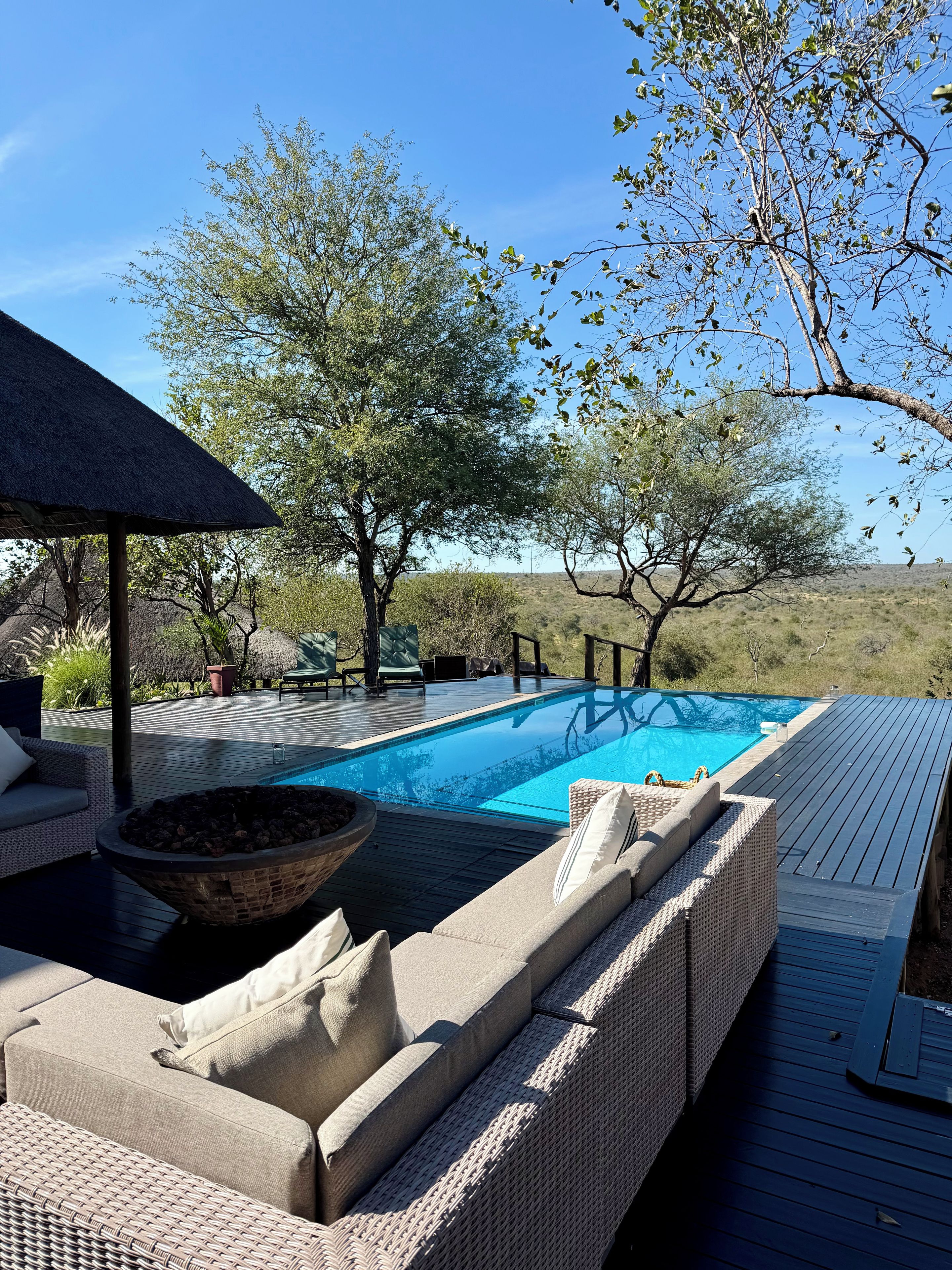 Una piscina con terraza, sillas de descanso y un hogar para la leña.