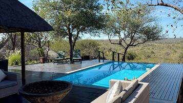 Una piscina con terraza, sillas de descanso y un hogar para la leña.